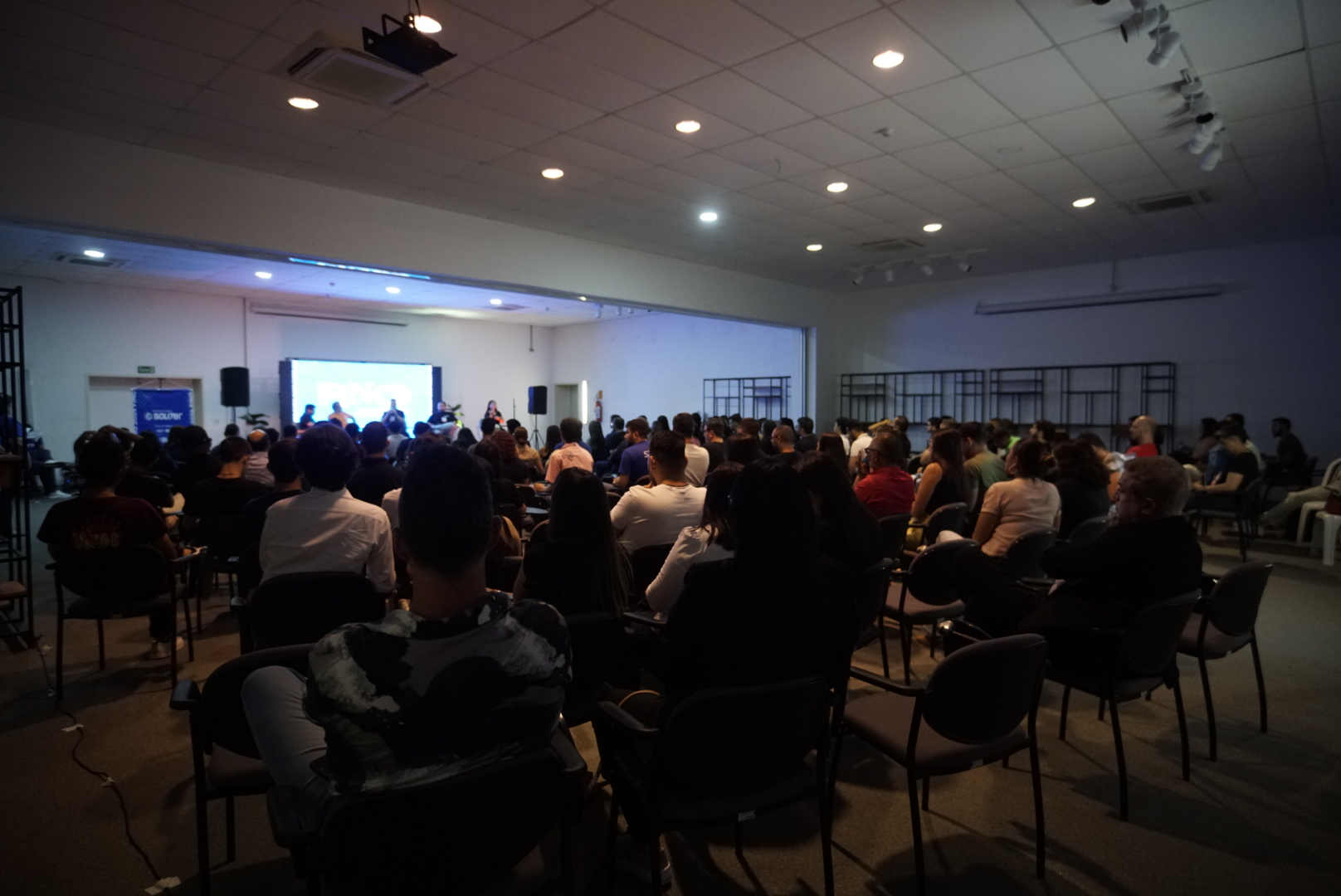 Sala lotada acompanhando uma apresentação no telão