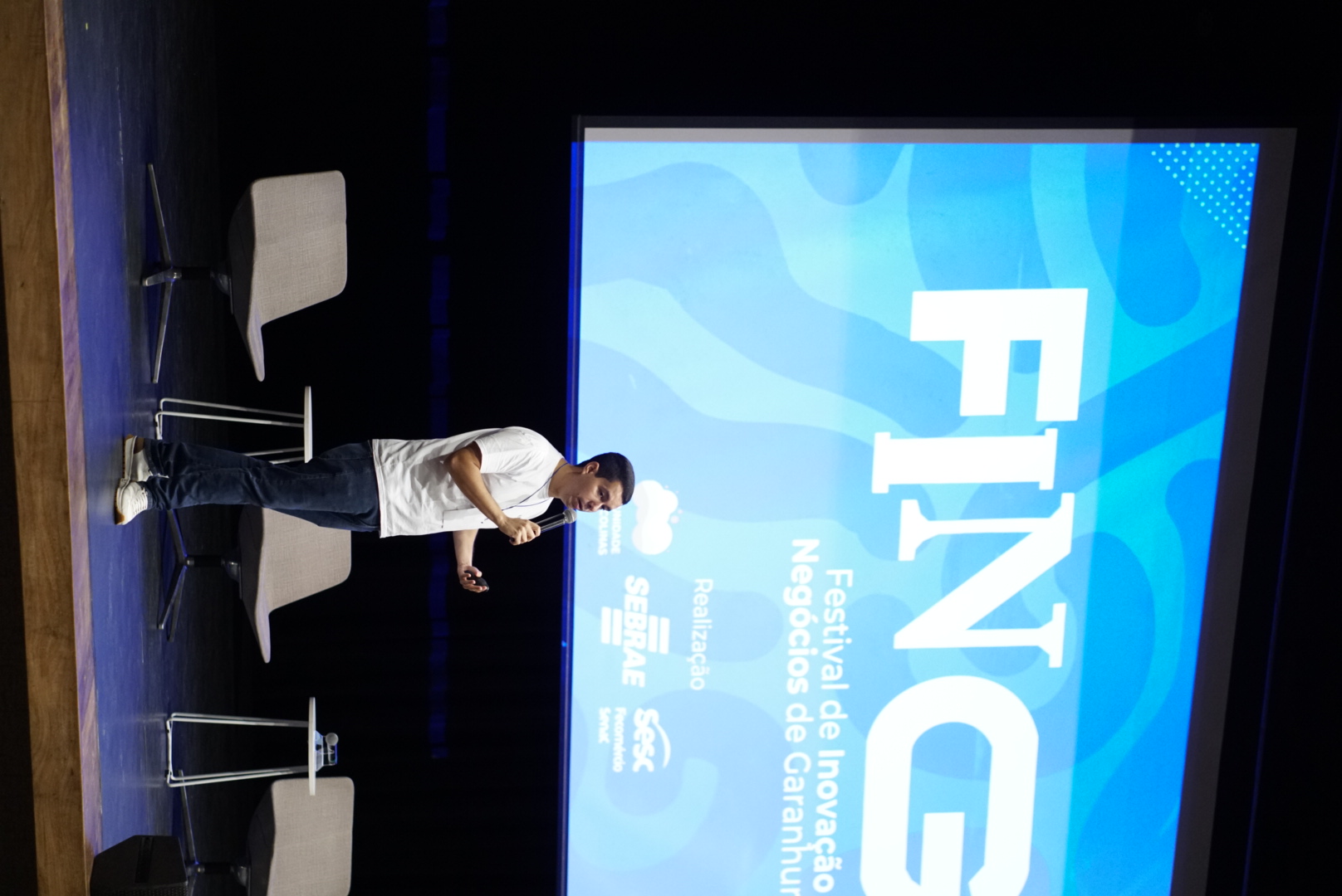 Palestrante no palco do FING com o telão do festival ao fundo